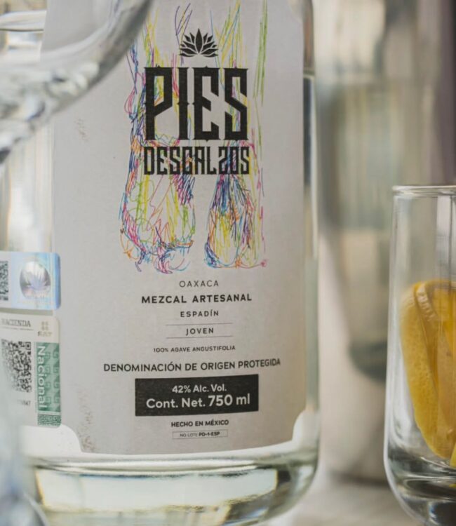 Pies Descalzos — El mezcal que se camina. El nombre nace de algo real: un maestro mezcalero subiendo un cerro, cargando garrafas vacías y...