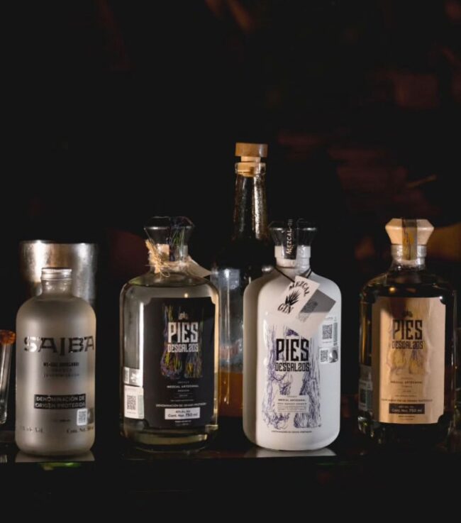 Pies Descalzos — El mezcal que se camina. El nombre nace de algo real: un maestro mezcalero subiendo un cerro, cargando garrafas vacías y...